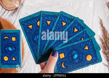 La mano con le unghie blu regge le carte dei Tarocchi sventolate su un foglio di tessuto bianco con gli spikelets. Minsk, Bielorussia - 09.27.2021 Foto Stock