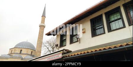 Sarajevo, Bosnia ed Erzegovina, 8 marzo 2020, un vecchio edificio commerciale in stile turco con la moschea principale e il minareto sullo sfondo. Gazi Husrev-begova dzamija. Torre di una moschea Foto Stock