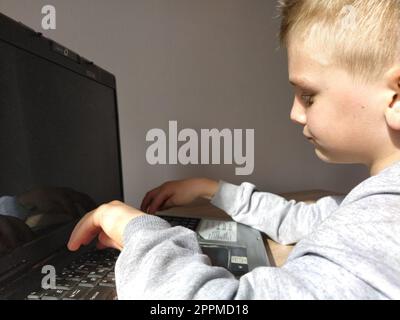 Sremska Mitrovica, Serbia, 20 maggio 2020 ragazzo biondo con portatile. Il bambino guarda il monitor e digita i tasti Foto Stock