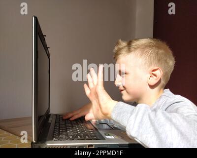 Sremska Mitrovica, Serbia, 20 maggio 2020 ragazzo biondo con portatile. Il bambino guarda il monitor e agita la mano come un saluto Foto Stock