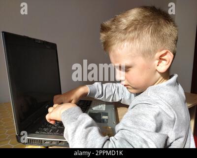 Sremska Mitrovica, Serbia, 20 maggio 2020 ragazzo biondo con portatile. Il bambino guarda il monitor e digita i tasti Foto Stock