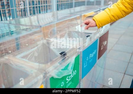Primo piano ritratto ritagliato di qualcuno donna mano getta un tovagliolo di carta usato nella spazzatura può in città strada. Smistamento dei rifiuti, contenitore di riciclaggio Foto Stock