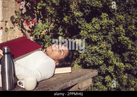 donna latina che dorme al sole con un libro Foto Stock
