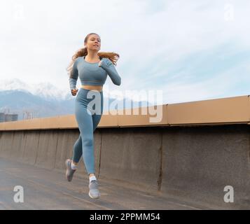 Donna atletica è in esecuzione sul tetto del parcheggio, garage su sfondo tramonto. Foto Stock