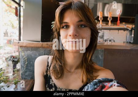 selfie ritratto di giovane donna transgender latina di etnia argentina, seduta in un ristorante in argentina, guardando la macchina fotografica al chiuso, persone Foto Stock