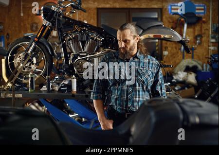 Ritratto di bearded brutale biker a moto in officina garage Foto Stock