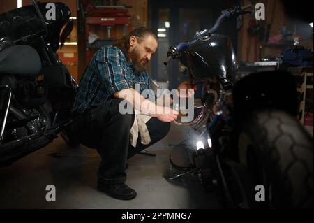 Uomo maturo biker riparazione moto in garage di sera Foto Stock