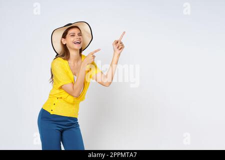 Giovane donna che indossa un cappello da sole e che indica uno spazio vuoto di copia isolato su sfondo bianco. Foto Stock