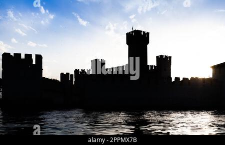 Italia - Castello di Sirmone silhouette sul lago di Garda al tramonto. Architettura medievale con torre. Foto Stock