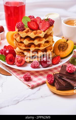 Waffle belgi con fragole, albicocche, ciliegie, succo di frutta e una tazza di caffè nero Foto Stock