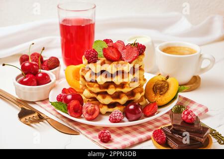 Waffle belgi con fragole, albicocche, ciliegie, succo di frutta e una tazza di caffè nero Foto Stock