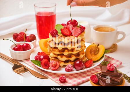 Waffle belgi con fragole, albicocche, ciliegie, succo di frutta e una tazza di caffè nero Foto Stock