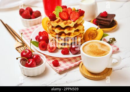 Waffle belgi con fragole, albicocche, ciliegie, succo di frutta e una tazza di caffè nero Foto Stock