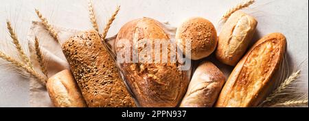 Assortimento di vari deliziosi pane appena sfornato, banner. Varietà di composizione artigianale del pane e spighe di grano. Foto Stock