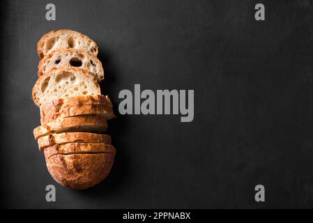 Pane di pasta alimentare artigianale appena sfornato. Pane affettato su fondo nero, spazio copia. Foto Stock