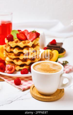 Waffle belgi con fragole, albicocche, ciliegie, succo di frutta e una tazza di caffè nero Foto Stock