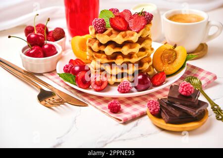 Waffle belgi con fragole, albicocche, ciliegie, succo di frutta e una tazza di caffè nero Foto Stock