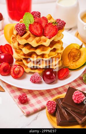 Waffle belgi con fragole, albicocche, ciliegie, succo di frutta e una tazza di caffè nero Foto Stock