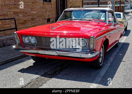 Un rosso luminoso completamente restaurato alle condizioni originali all'inizio degli anni '60 Plymouth sport fury cabriolet top 2 porte parcheggio accanto a un edificio in un'esposizione di auto su un Foto Stock