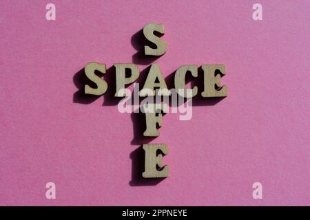 Safe, spazio, parole in lettere alfabetiche di legno in forma di croce isolato su sfondo rosa brillante Foto Stock