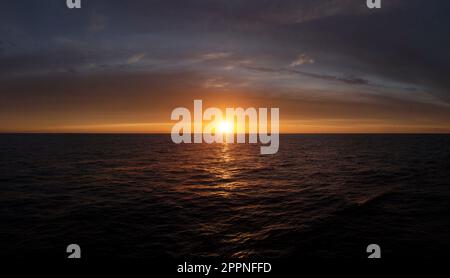 Tramonto sull'oceano, il caldo bagliore del sole della sera che si riflette sulle onde del mare e alcune nuvole nel cielo, sul Mare del Nord Foto Stock