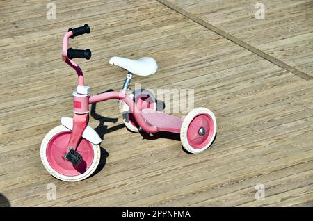 Triciclo rosa per bambini piccoli per giocare e trasportare all'aperto su un'area giochi in legno. Foto Stock