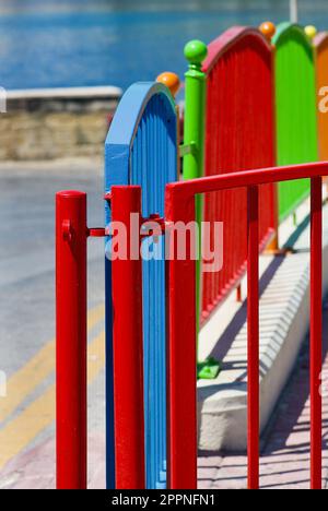 Recinzione colorata dipinta in diversi colori che racchiude un parco giochi all'aperto per bambini sull'isola di Malta. Foto Stock