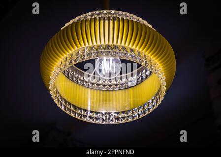 Interior design: Lampada da soffitto rotonda gialla in plastica con elementi in cristallo nello stile degli anni '1950s di fronte a uno sfondo scuro Foto Stock