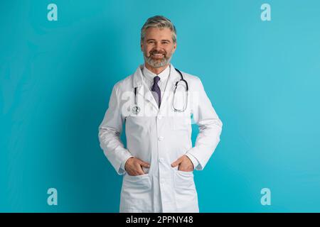 Ritratto di un bel medico europeo positivo in posa su blu Foto Stock