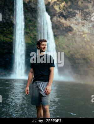 Uomo in piedi di fronte alla cascata di Wailua a Kauai, Hawaii. Foto di alta qualità. Situato nel Parco Statale del Fiume Wailua. Viaggi hawaiani Foto Stock