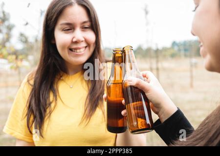 Primo piano di due amiche latine che fanno un brindisi con le birre in campagna. Foto Stock