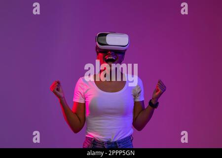 Overjoyed Young Black Female indossa occhiali VR per celebrare il successo in Neon Light Foto Stock