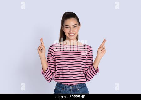 Giovane donna sorridente che tiene le dita incrociate per buona fortuna Foto Stock