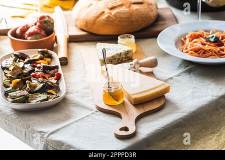 Tavolo con un piatto di formaggio e marmellata, spaghetti con salsa di pomodoro e basilico, verdure alla griglia. Luce del tramonto che illumina la stanza Foto Stock