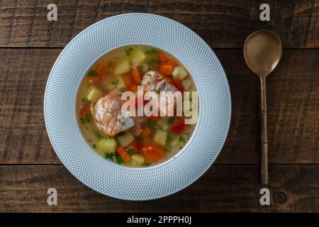 Zuppa di salmone fresco con carote, patate e peperoni rossi in un piatto bianco su tavolo di legno, primo piano. La cena gustosa consiste in una zuppa di pesce con sa Foto Stock