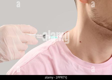 Dermatologo prendendo la puntura di talpa da giovane uomo su sfondo grigio, primo piano Foto Stock