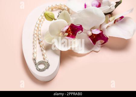 Vetrina piedistallo con collana in perla e fiori orchidee su sfondo rosa, primo piano Foto Stock