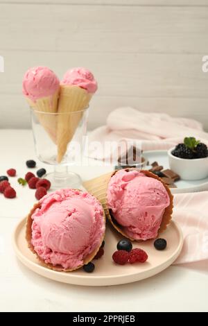 Delizioso gelato rosa in cialda di wafer con bacche su tavola di legno bianco Foto Stock