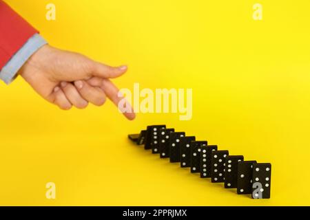 Donna che causa la reazione a catena spingendo tessera domino su sfondo giallo, primo piano Foto Stock