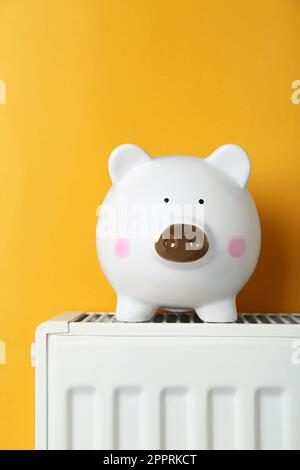 Banco di piggy sul radiatore di riscaldamento su sfondo arancione Foto Stock