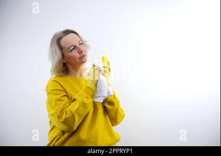 Bella donna anziana, in una T-shirt gialla e guanti di gomma su sfondo giallo con detergente. Foto di alta qualità Foto Stock