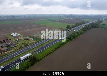 Piacenza, Italia - Aprile 2023 autocarri e auto da carico in autostrada del sole A1 punto di vista aereo tra pianura padana e campi rurali Foto Stock