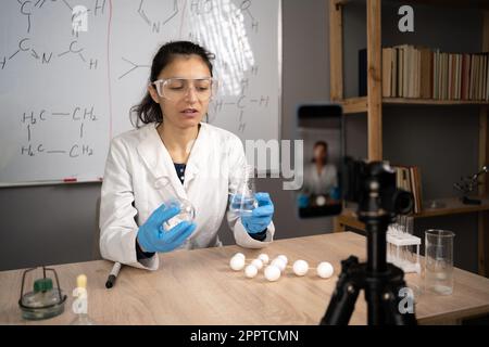 Motivata insegnante di sesso femminile ispanico blogger registrare video o storie su smartphone fotocamera, parlare di chimica scienza streaming online, videoblog Foto Stock