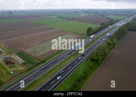 Piacenza, Italia - Aprile 2023 autocarri e auto da carico in autostrada del sole A1 punto di vista aereo tra pianura padana e campi rurali Foto Stock