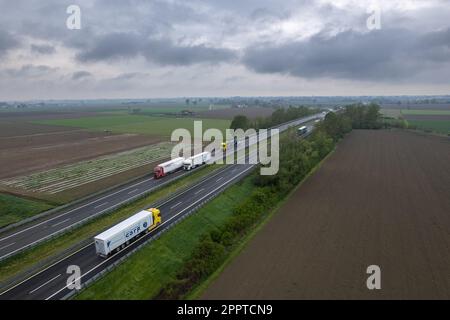 Piacenza, Italia - Aprile 2023 autocarri e auto da carico in autostrada del sole A1 punto di vista aereo tra pianura padana e campi rurali Foto Stock