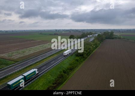 Piacenza, Italia - Aprile 2023 autocarri e auto da carico in autostrada del sole A1 punto di vista aereo tra pianura padana e campi rurali Foto Stock