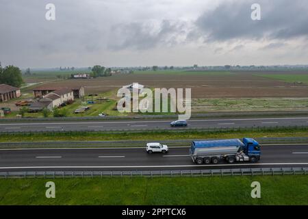 Piacenza, Italia - Aprile 2023 autocarri e auto da carico in autostrada del sole A1 punto di vista aereo tra pianura padana e campi rurali Foto Stock