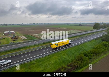 Piacenza, Italia - Aprile 2023 autocarri e auto da carico in autostrada del sole A1 punto di vista aereo tra pianura padana e campi rurali Foto Stock