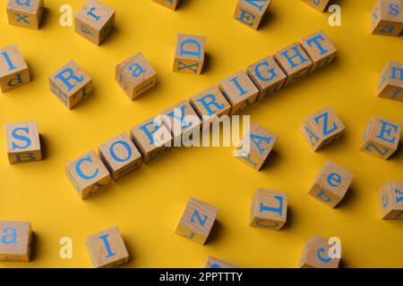 Concetto di plagio. Copyright di parole fatto di cubi di legno con lettere su sfondo giallo Foto Stock