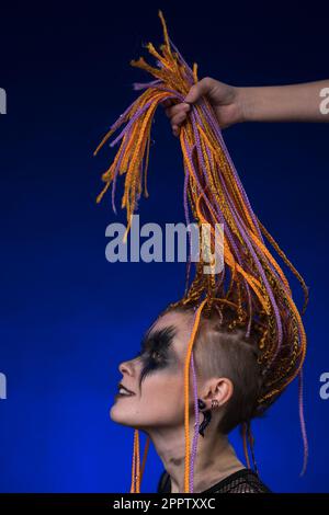 Fine arte ritratto di bella giovane donna con colore arancione Dreadlocks acconciatura e horror nero palco trucco dipinto sul viso. Monolocale con vista laterale Foto Stock